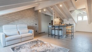 Un espacio tipo loft con zona de estar, sofá, cocina con taburetes y un ventanal grande.
