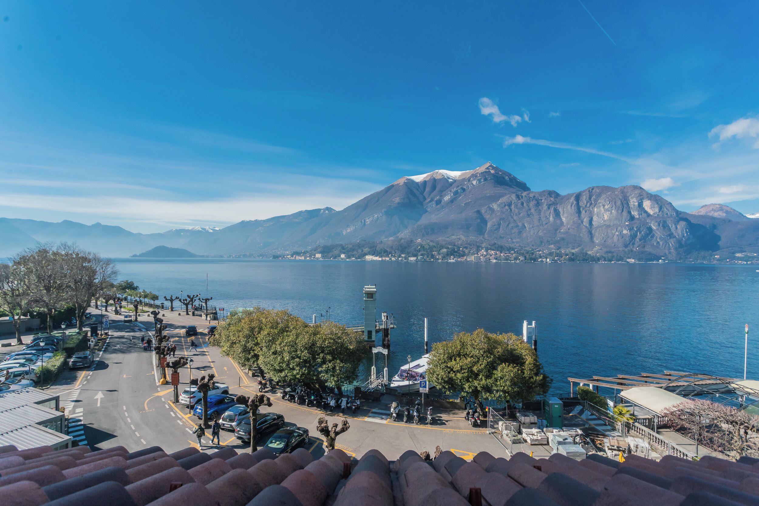 Vista costera con montañas, un área de estacionamiento y un paseo marítimo.