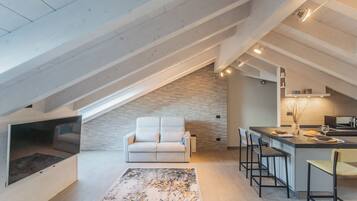 Un loft moderno con techo inclinado, sofá blanco, isla de cocina y ventana grande.