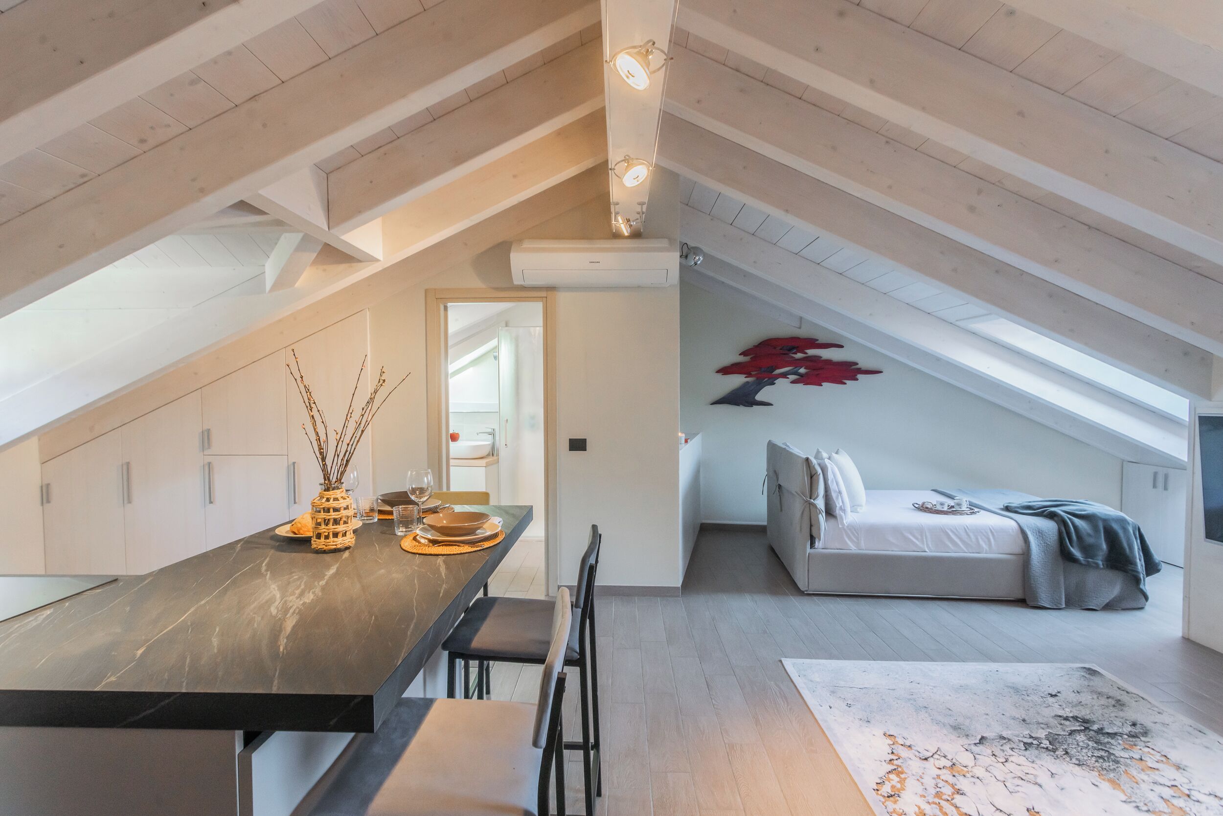 Un dormitorio tipo loft moderno con techo inclinado, una cama y un comedor con mesa y sillas.