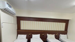 A hotel room with four single beds, a patterned floor, a headboard with vertical stripes, and an air conditioning unit. - MEHAD MADINAH QUBA (Madinah)