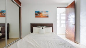 Een slaapkamer met een bed, een houten hoofdbord, een grote spiegel en een schilderij aan de muur.