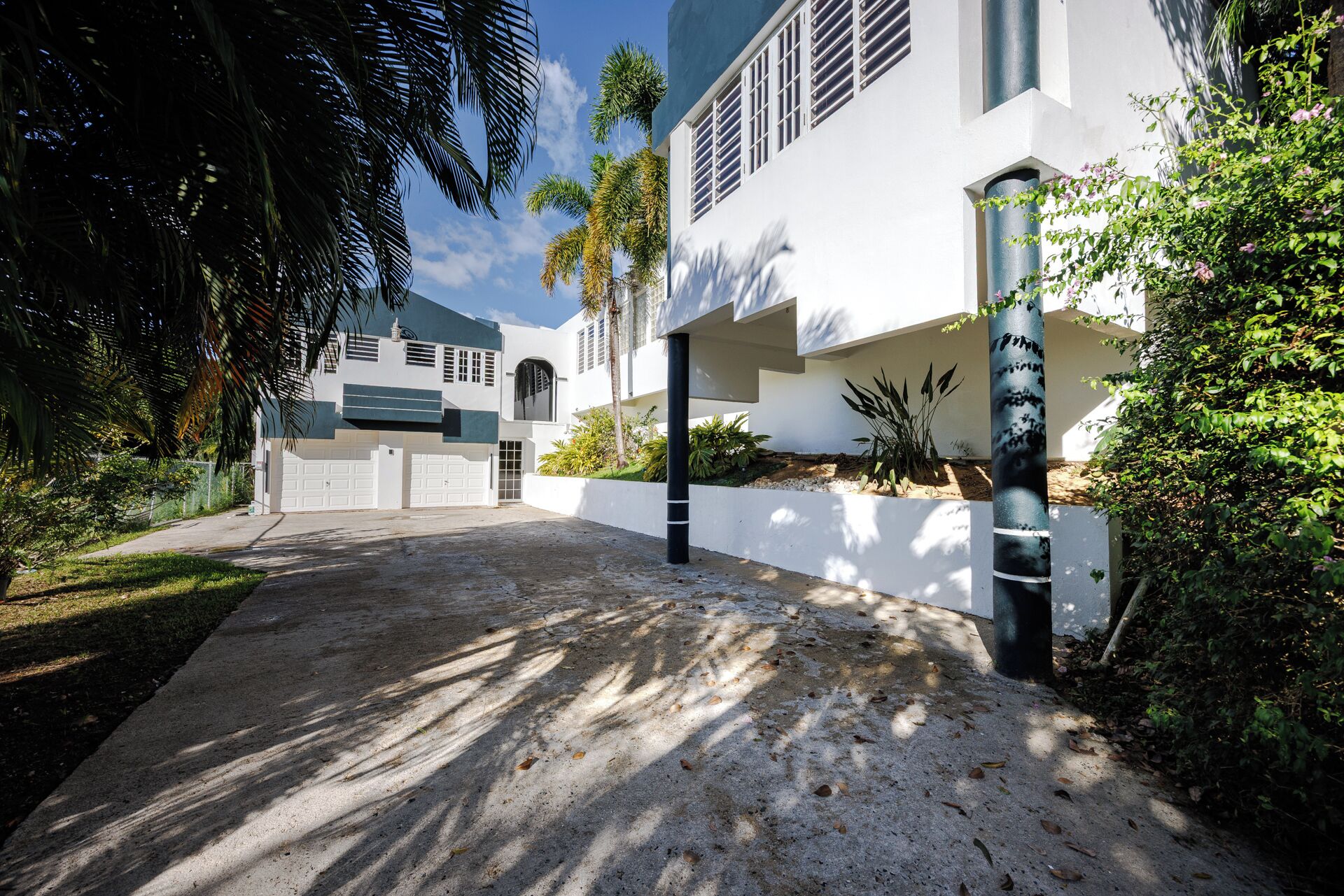 Uma casa moderna de dois andares com garagem, rodeada por vegetação exuberante e palmeiras.