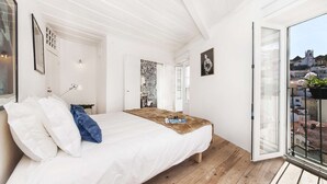 Een slaapkamer met een bed, een houten vloer, een witte muur, een deur en een balkon met uitzicht.