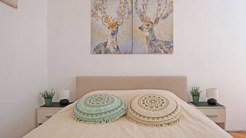 A bed with two decorative pillows, a nightstand with a plant and a lamp, and a painting of deer on the wall.