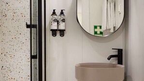 Ein Badezimmer mit einem runden Waschbecken, einem Spiegel und zwei Handdesinfektionsspendern.