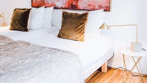 Un dormitorio con una cama grande, ropa de cama blanca, piso de madera, una lámpara moderna y un cuadro abstracto grande en la pared.