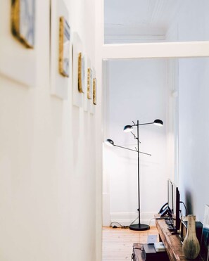 Ein Zimmer mit Schreibtisch, Lampe, einer Vase und gerahmten Bildern an der Wand.