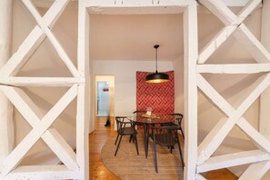 A room with a white geometric wall structure, a round table with chairs, and a hanging light fixture. - Cheese&Wine™ | Alfama - Sé Cathedral 2 (Lisboa)