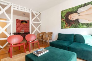 Ein Wohnzimmer mit einem grünen Sofa, roten Stühlen, einem Essbereich mit einer Wand mit Muster und einem Gemälde einer Person an der Wand.
