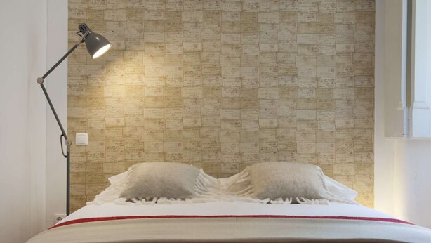 Ein Bett mit zwei Kissen, einer roten Decke und einer Wand mit ornamentalem Wandpapier.