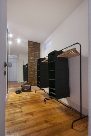 A hallway with a wooden floor, a mirror, a black coat rack, and a black shelving unit. - Cheese&Wine™ | Chiado - Rossio Square 1 (Lisboa)