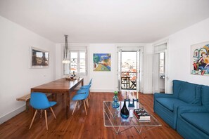A modern living space with a wooden dining table, blue chairs, a glass coffee table, and a blue sofa. - Cheese&Wine™ | Chiado - Rossio Square 1 (Lisboa)