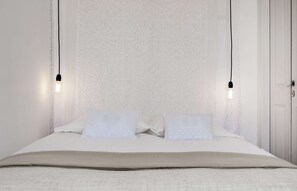 A bed with two pillows, a white wall with a geometric pattern, and two hanging light bulbs. - Cheese&Wine™ | Chiado - Rossio Square 1 (Lisboa)