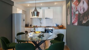 A modern kitchen with white cabinets, a glass dining table, and green chairs. - Cheese&Wine™ | Chiado - Rossio Square 2 (Lisboa)