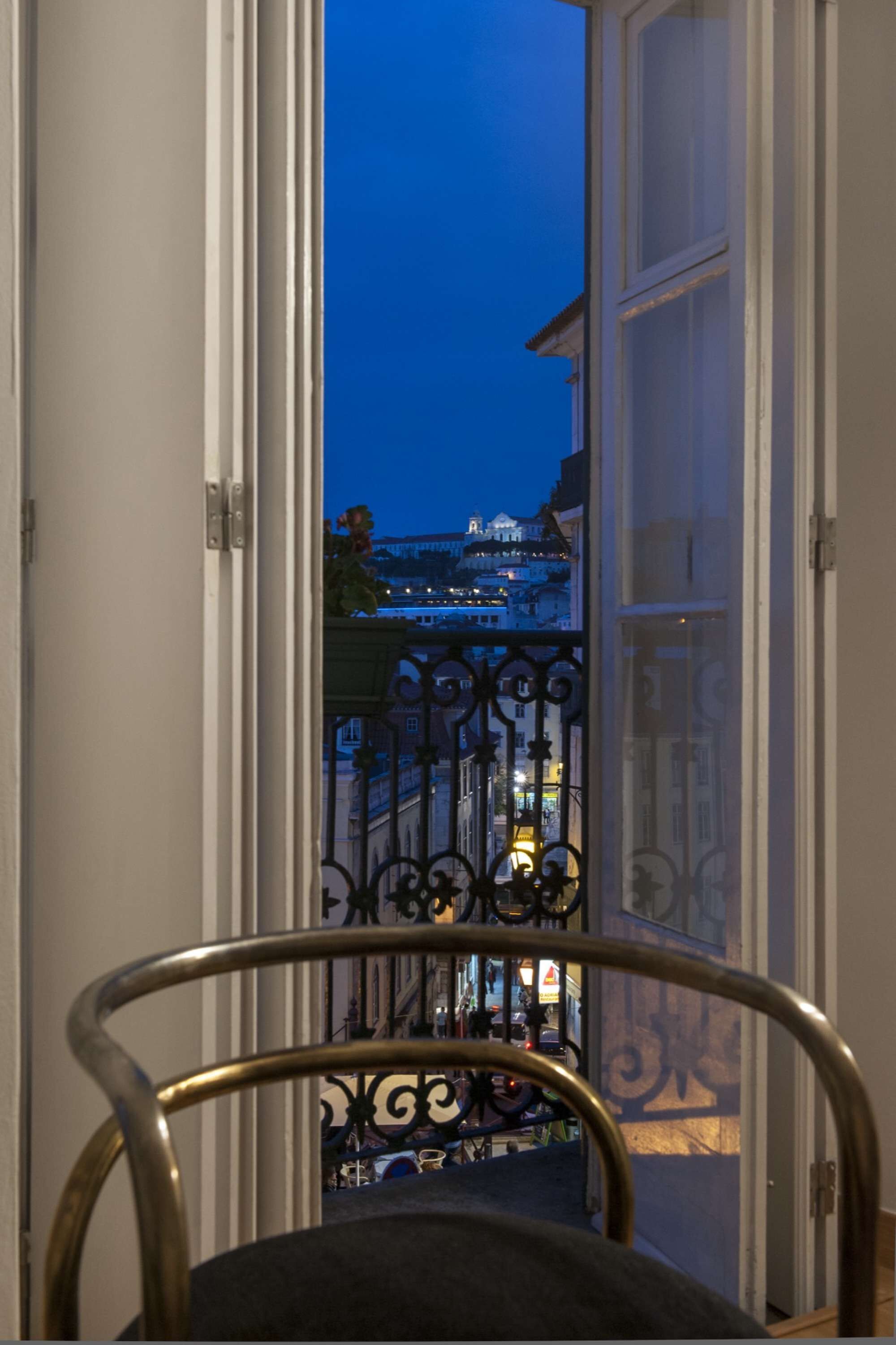 Uitzicht vanaf een balkon met een metalen hekwerk, op een stadsgezicht tijdens de schemering.