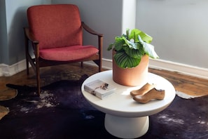 Ein Zimmer mit einem roten Sessel, einem runden weißen Tisch mit Pflanze und Buch sowie einem Kuhfellteppich.