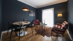 A dining area with a round table, chairs, a red pendant light, a red armchair, a patterned armchair, a glass vase, and a fur rug. - Cheese&Wine™ | Sra. do Monte - Viewpoint 1 (Guest Favorite) (Lisboa)