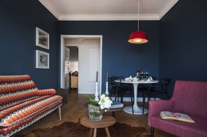 Ein Wohnzimmer mit einer Couch, einem runden Tisch mit Stühlen, einer roten Pendelleuchte und einer Tür zu einem anderen Raum.