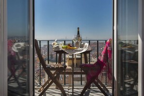 Un balcon avec une table dressée pour deux personnes, une bouteille et une chaise recouverte d’un tissu.
