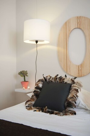 Ein Bett mit einem schwarzen Kopfkissen, einer runden Holz-Wanddekoration, einer Stehlampe und einem kleinen Topfpflanzen auf einem weißen Nachttisch.