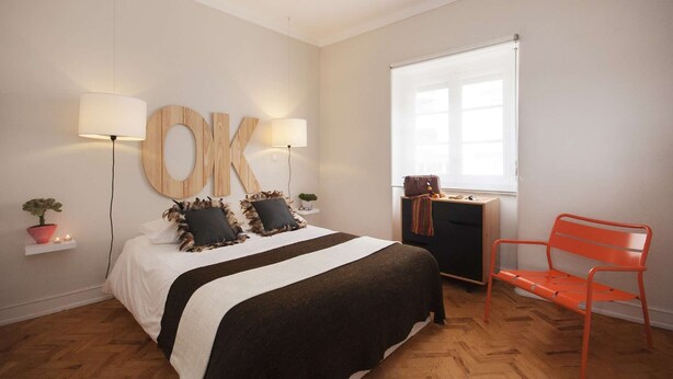 A bedroom with a bed, two wall-mounted lamps, a window, a desk, a chair, and a large 'OK' sign on the wall. - Cheese&Wine™ | Sra. do Monte - Viewpoint 1 (Guest Favorite) (Lisboa)