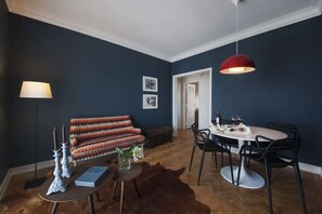 Ein modernes Wohnzimmer mit einer Couch, einem Esstisch mit Stühlen, einer roten Pendelleuchte und einer Stehlampe.