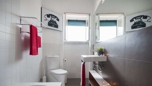 A modern bathroom with a white toilet, a bathtub, a sink with a mirror, and two windows. - Cheese&Wine™ | Sra. do Monte - Viewpoint 1 (Guest Favorite) (Lisboa)