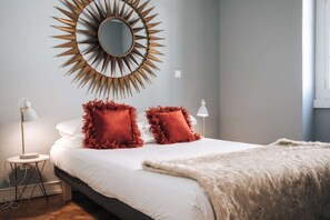 Ein Schlafzimmer mit einem Bett, zwei roten Kissen, einer flauschigen weißen Decke, einem runden Spiegel und zwei Nachttischlampen.