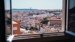 A cityscape with a prominent bridge in the distance, viewed through a window. - Cheese&Wine™ | Sra. do Monte - Viewpoint 3 (Lisboa)
