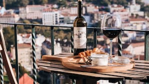 A balcony with a table set for a meal, a bottle of wine, and a glass of wine. - Cheese&Wine™ | Sra. do Monte - Viewpoint 3 (Lisboa)