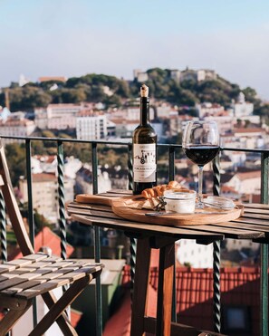 Ein Balkon mit Tisch, gedeckt für eine Mahlzeit, einer Weinflasche und einem Weinglas.