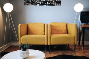 Ein Wohnzimmer mit einer Couch, zwei Stehlampen, einem kleinen Tisch mit Pflanze und einem Fernseher.
