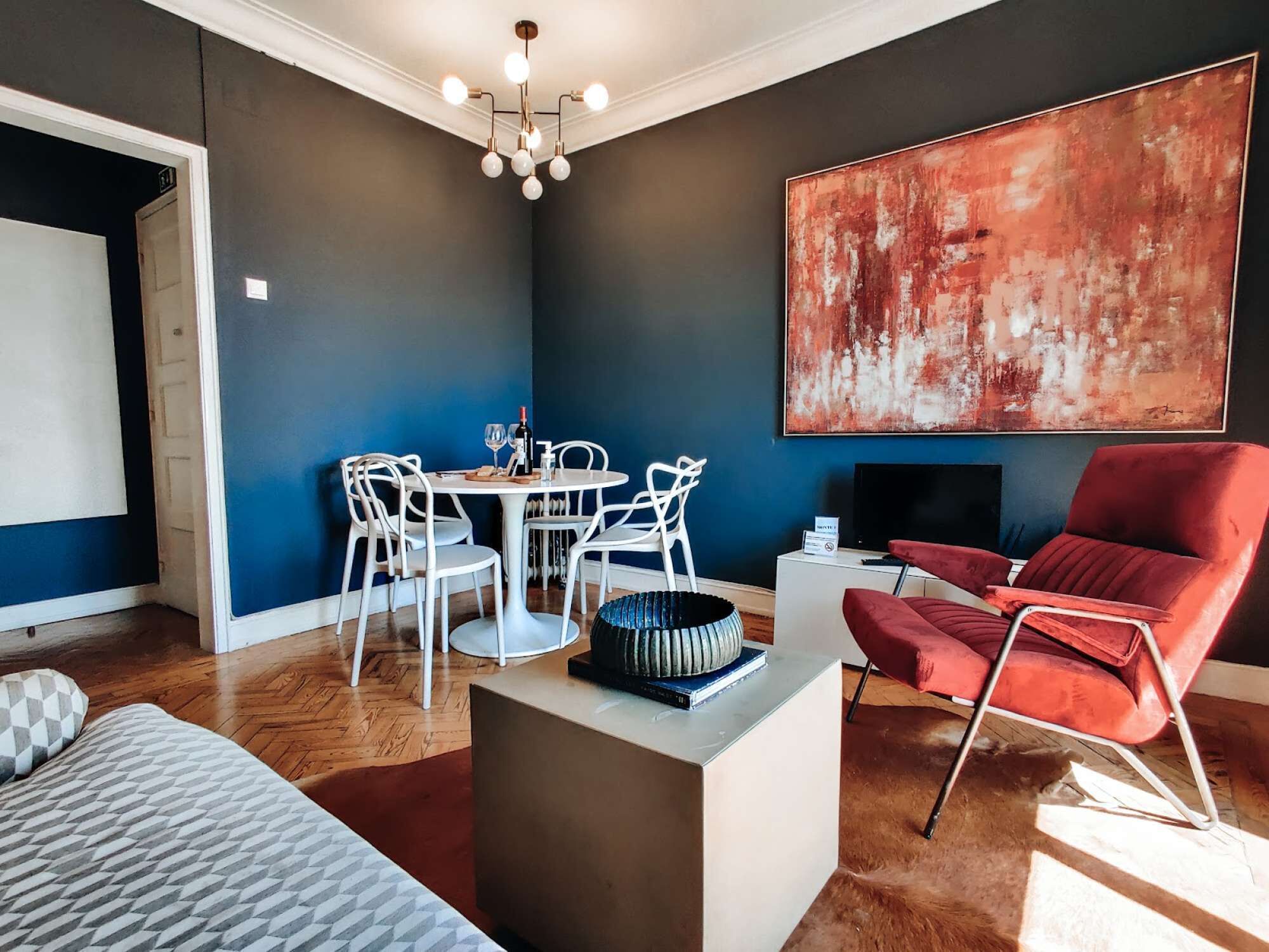 A modern living room with a dining area, a red armchair, a large abstract painting, and a chandelier.