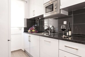 Eine moderne Küche mit weißen Schränken, einer Edelstahl-Mikrowelle, einem Spülbecken mit Wasserhahn und einer Weinflasche auf der Arbeitsplatte.