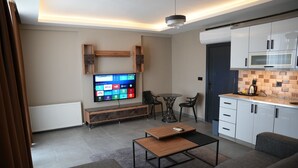 A modern living room with a flat-screen TV, a sofa, a coffee table, and a dining area with chairs. - Atlas Suit Otel (mersin)
