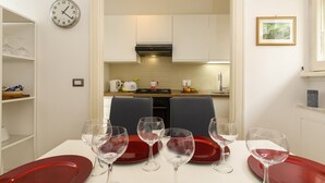 A dining area with a table set for four, a kitchen in the background, and a clock on the wall. - Bernini Alle Fornaci - St Peter Vatican (Rome)