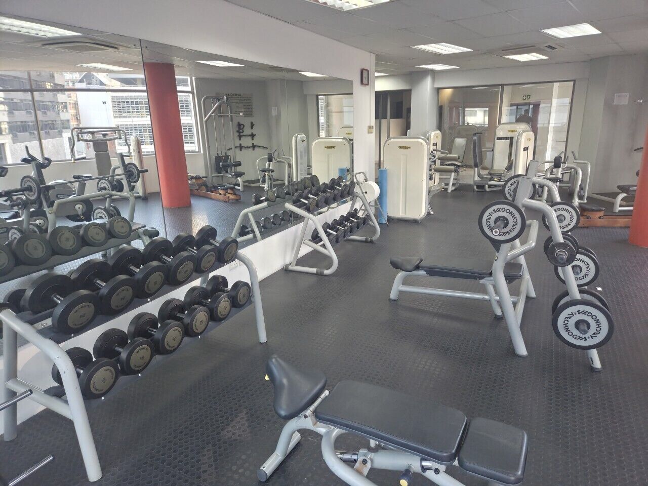 A gym with weightlifting equipment, benches, and a mirrored wall.