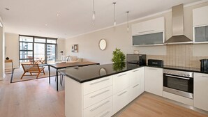 Una cocina moderna con armarios blancos, encimera negra, horno Bosch y un comedor con mesa y sillas.