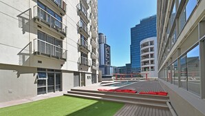 Un edificio moderno con varios pisos, balcones y una terraza en la azotea con piscina y asientos rojos.