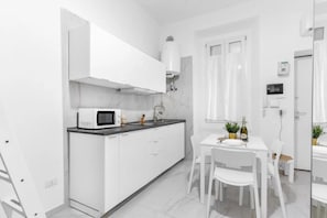 A compact kitchen with white cabinets, a microwave, a sink, and a small dining area with a table and chairs. - ARQ16 [Cathedral-Loreto] • Central • Modern (Milano)