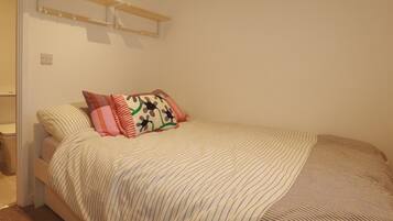 A bedroom with a bed, pillows, a bedside table, and a wall-mounted shelf.