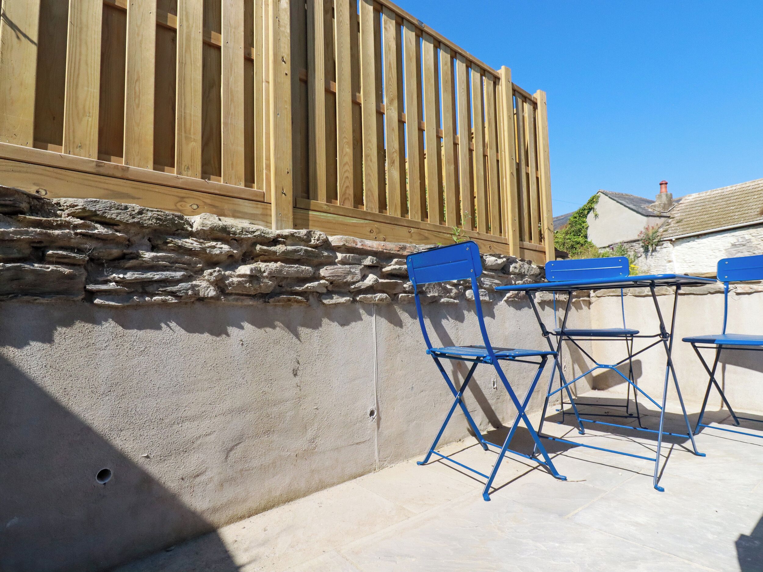 Une terrasse avec des murs en pierre, une clôture en bois et des chaises pliantes bleues.