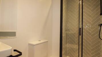 Un baño con inodoro, lavabo y ducha con mampara de vidrio.
