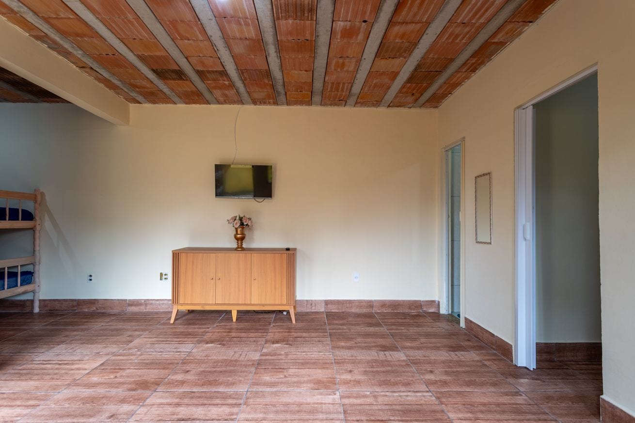 An empty room with a wooden cabinet, a television mounted on the wall, and a tiled floor.