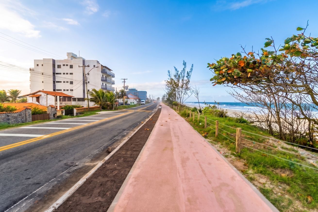 Uma estrada costeira com calçada, edifícios e uma praia ao longe.