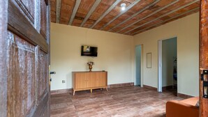 A room with a wooden floor, a wooden cabinet, a television mounted on the wall, and a door leading to another room. - Casa c Churrasqueira a 400m da Praia de Barra Nova (Saquarema)