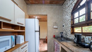A compact kitchen with a refrigerator, microwave, and coffee maker, wooden cabinets, and a window with a view. - Casa c Churrasqueira a 400m da Praia de Barra Nova (Saquarema)