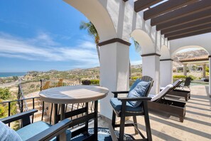Eine Terrasse mit einem runden Tisch und Stühlen, einer Pergola und Blick auf das Meer und die Hügel.