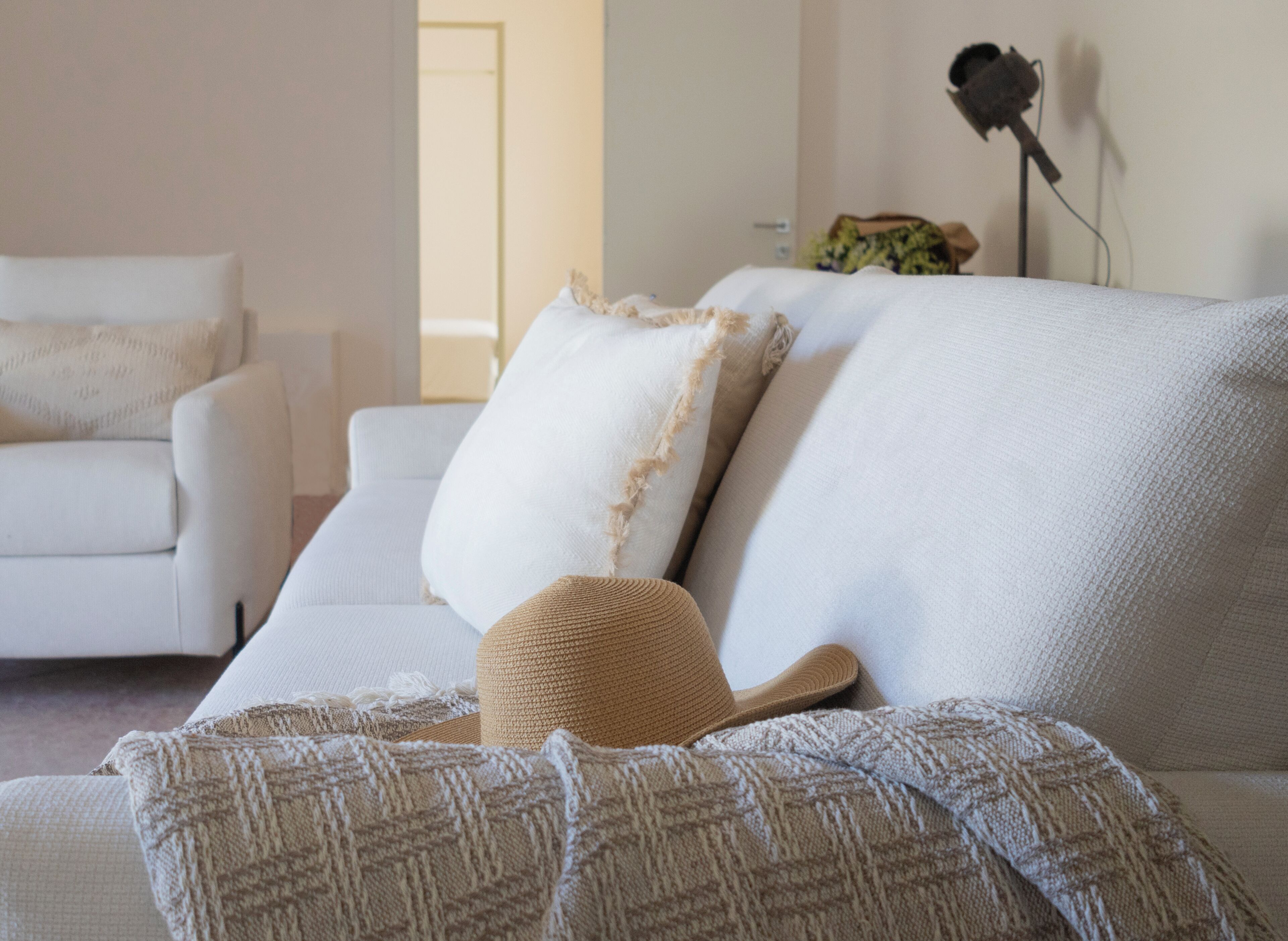 Ein weißes Sofa mit einer gemusterten Decke und einem gewebten Hut.
